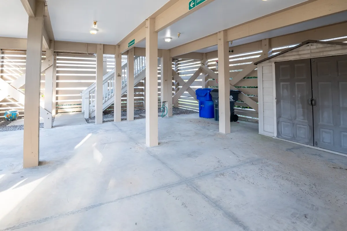 A functional entryway area featuring support beams, stairs, a storage shed, and a blue trash can. The space serves as a practical transition point for organizing gear and entering the home, hinting at the keyless entry feature and the ease of coming and going.