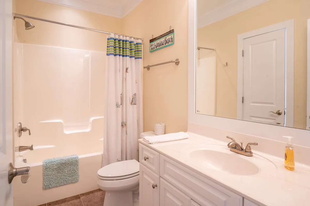 A clean, modern bathroom with a vanity, sink, toilet, bathtub with shower, decorative shower curtain, and mirror. The space feels light and refreshing, offering both functionality and comfort.