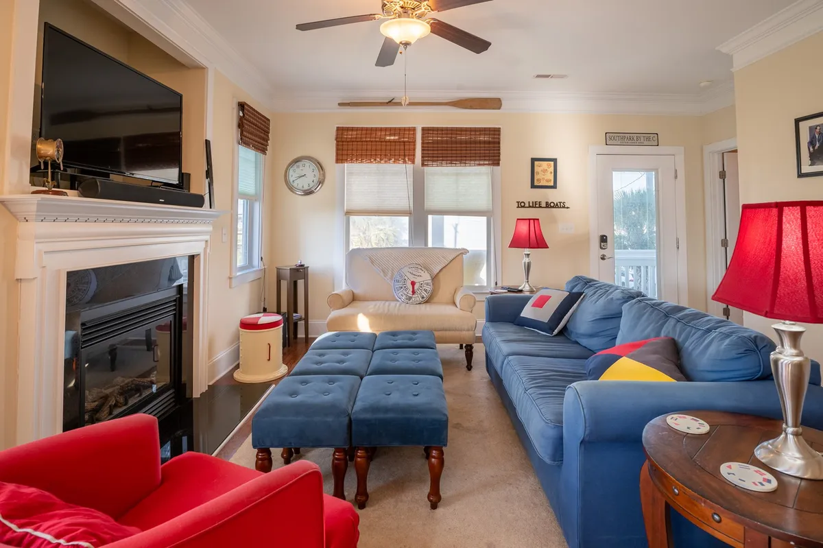 This image showcases a bright living room with a blue sofa, a red armchair, a coffee table, and a fireplace. Large windows allow an abundance of natural light to fill the space, suggesting an airy atmosphere and a strong connection to the outdoors.