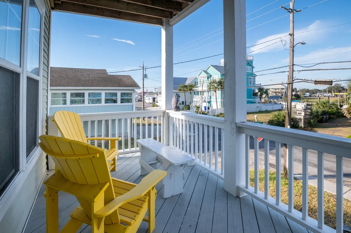 An exterior view highlighting yellow Adirondack chairs, a white bench, and a backdrop of blue sky. The setting suggests a communal outdoor area ideal for gathering with friends, enjoying sunsets, or prepping for a night on the town.