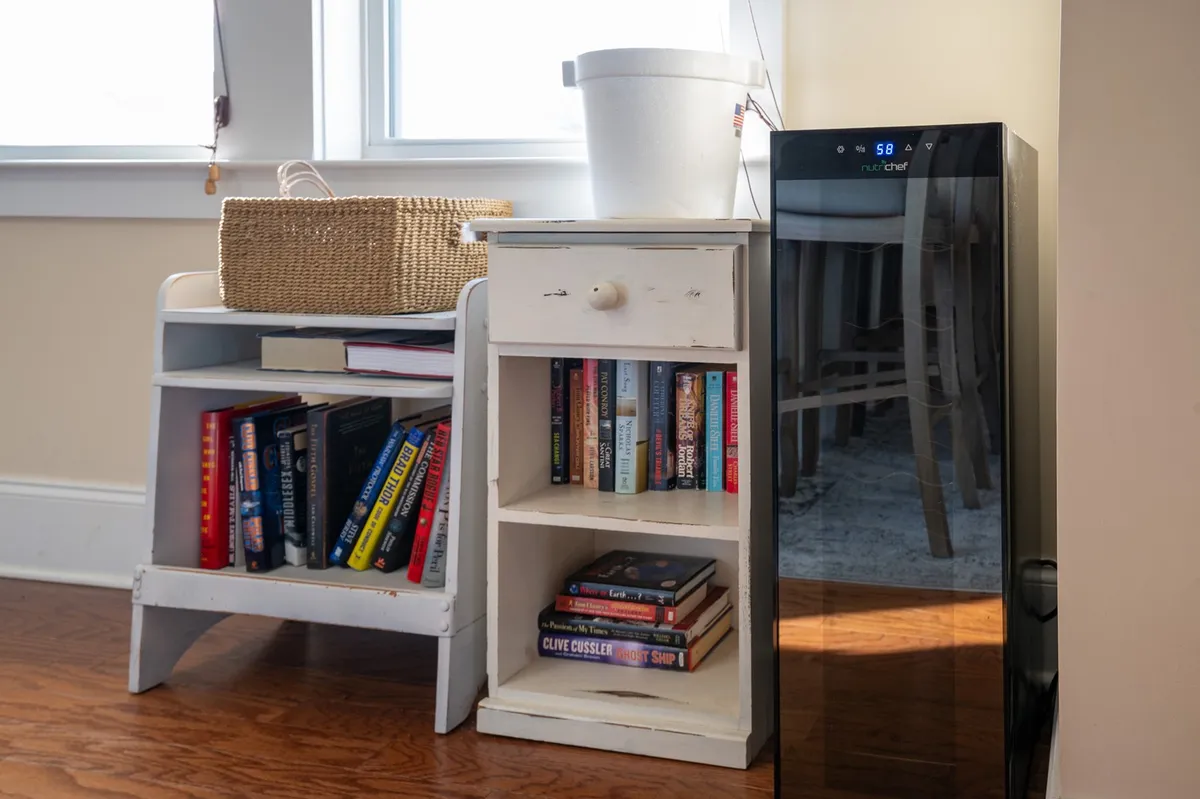 A cozy interior featuring a bookshelf and a wine cooler, with inviting baskets and soft seating that suggest opportunities for reading, relaxing, or intimate conversations over wine.