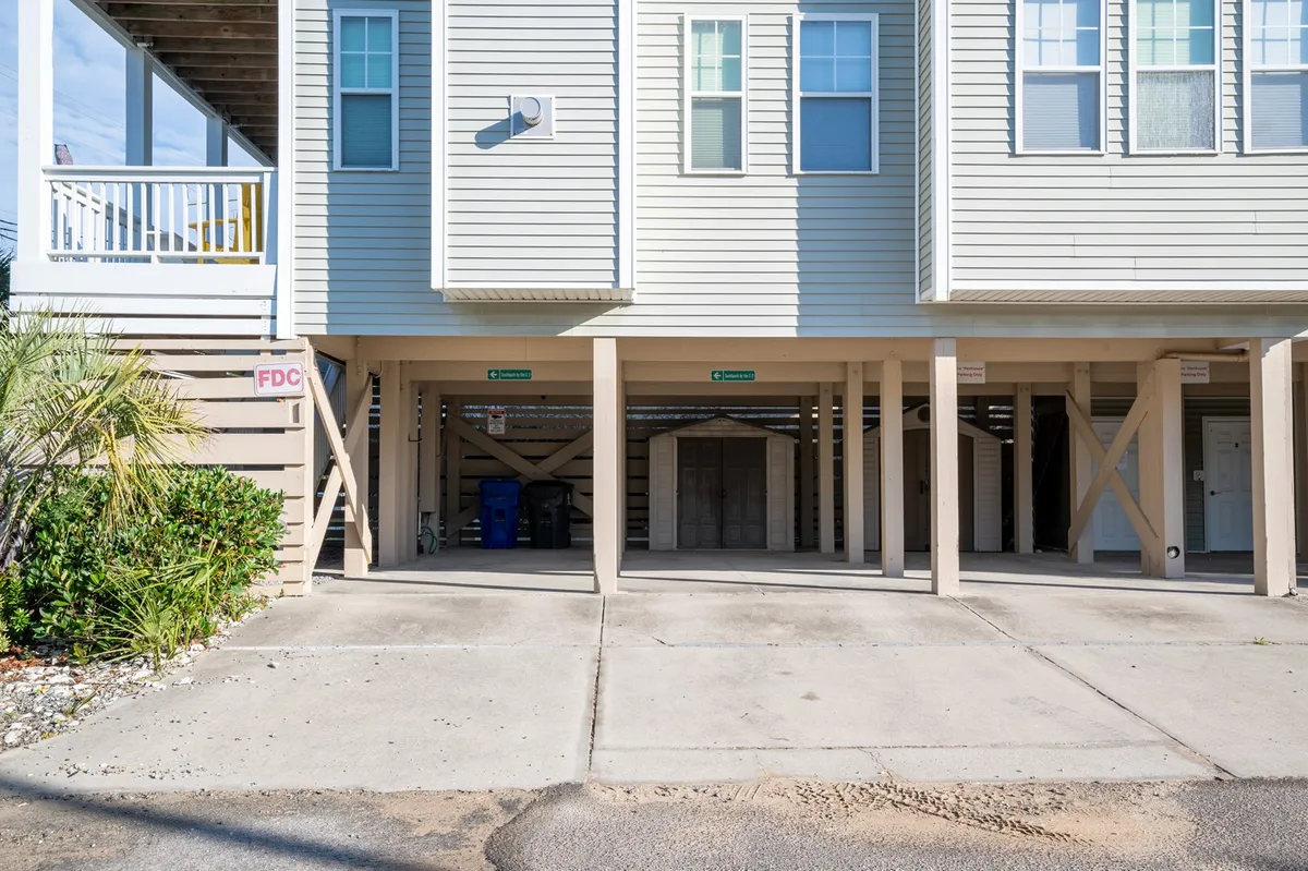 A view of the building’s exterior showing the structure, a palm tree, and the dedicated parking area. The open lot and proximity to the entryway emphasize convenient and secure assigned parking, with the beachy vibe of palm trees reinforcing the coastal setting.