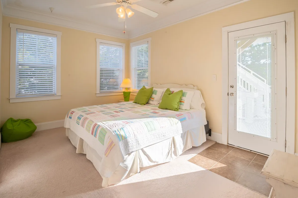 A cheerfully-lit bedroom with a colorful quilt, green accent pillows, and a door leading outside, suggesting easy transitions from private relaxation to outdoor adventures.