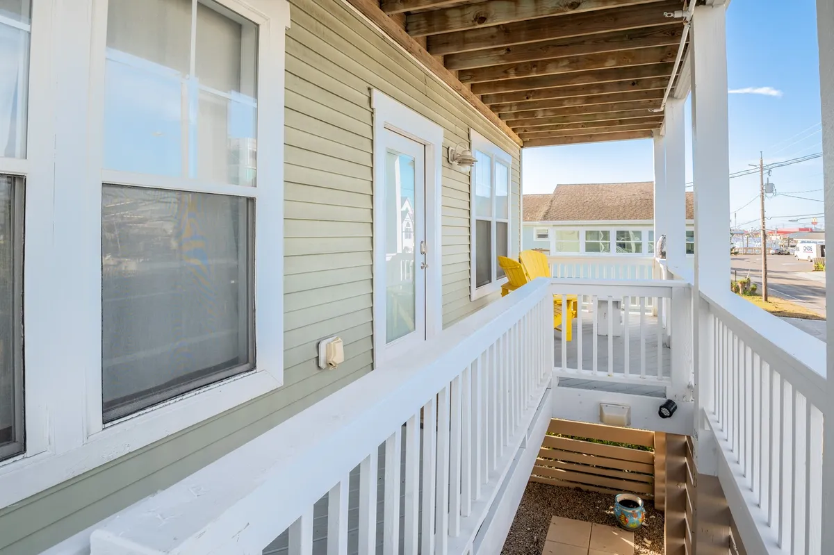 A cheerful exterior scene featuring two yellow chairs and a white railing on a porch, inviting guests to relax with friends or enjoy the lively street scene just beyond the doorway. The image captures the transition from a cozy home environment to the vibrant neighborhood.